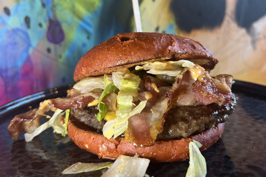 A hamburger featuring a red bun, beef patty, bacon, and lettuce on a plate.