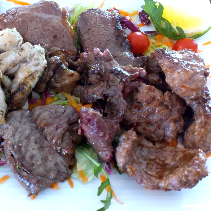 A platter featuring various grilled meats including beef and chicken, garnished with vegetables and lemon.