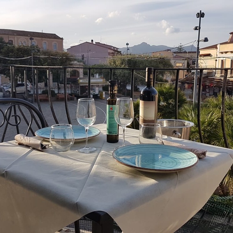 Table set with glasses, bottles, and plates on a balcony overlooking a plaza.