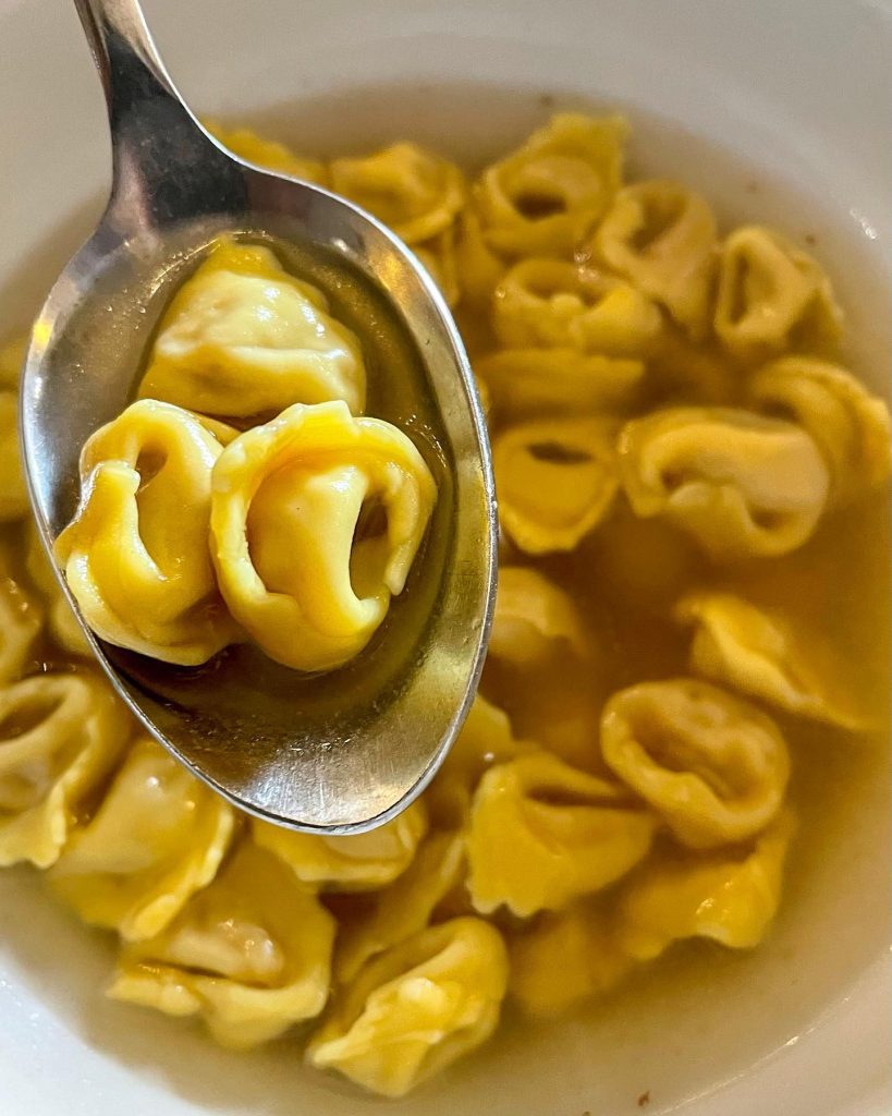 A spoonful of tortellini served in a clear broth, showcasing the pasta's shape and texture.