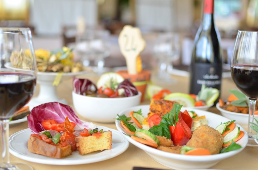 Plates of assorted Italian dishes including vegetables, bread, and wine on a table.