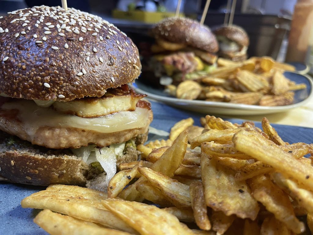 Close-up of a sesame seed burger with cheese and fries on a plate.