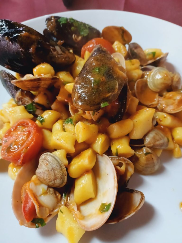 Plate of seafood pasta featuring clams, mussels, and cherry tomatoes with a sauce.
