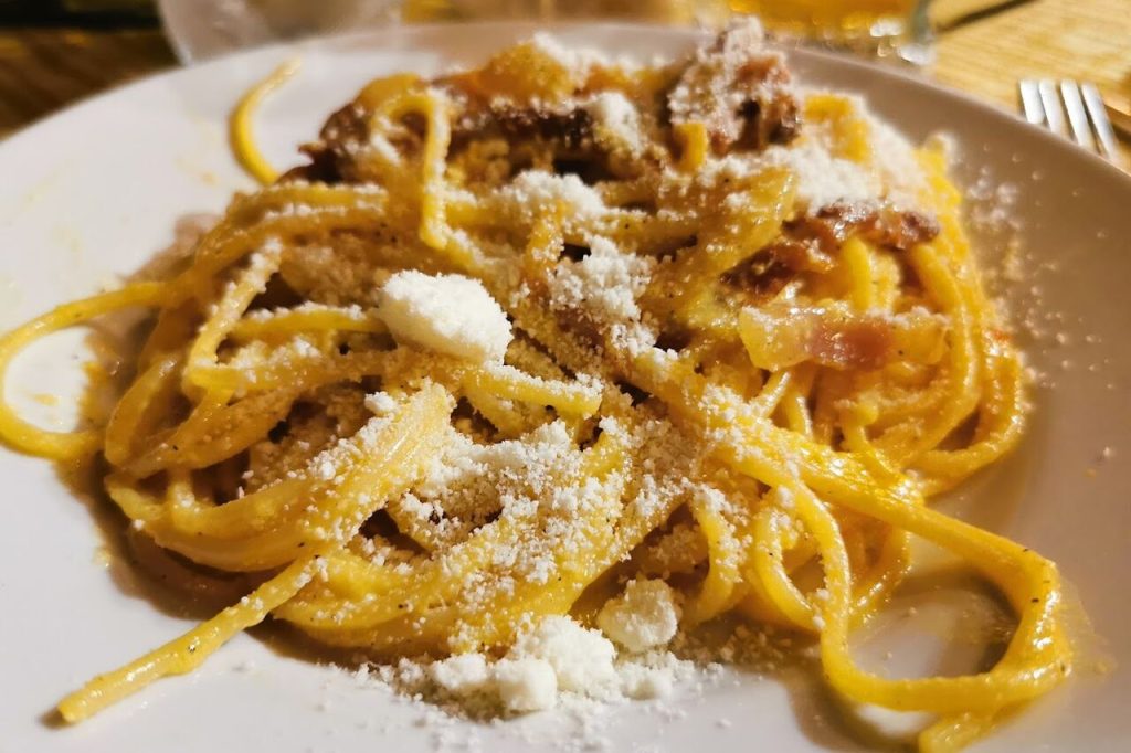Plate of spaghetti topped with grated cheese and bits of meat.