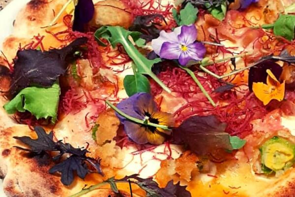 Gourmet pizza topped with edible flowers, greens, and various garnishes.