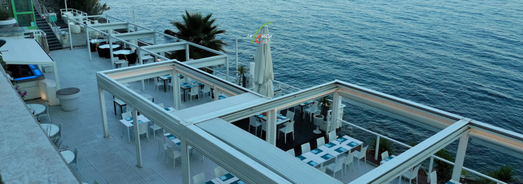 An outdoor dining area with white furniture and a view of the water in the background.