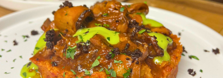 A plate of pasta topped with sauce, herbs, and a green garnish.