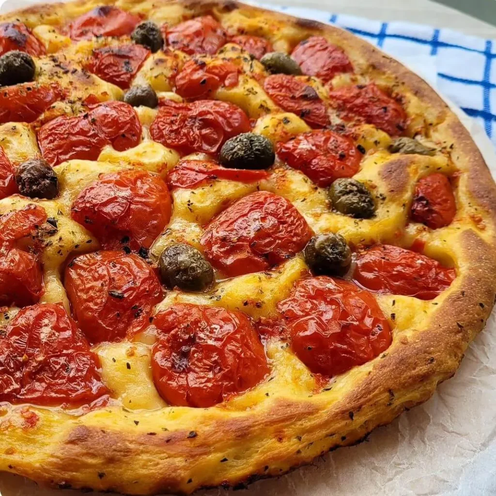 Focaccia Barese topped with cherry tomatoes and olives on a light background.